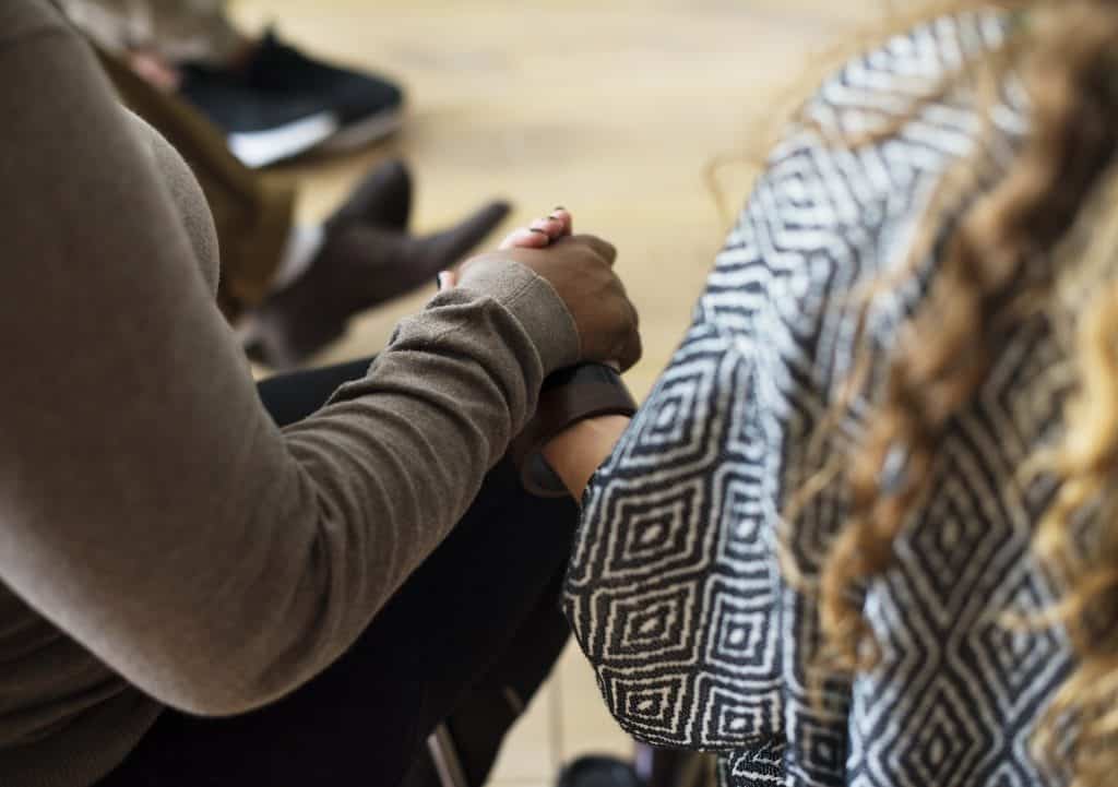 Two survivors sitting in a group hold hands