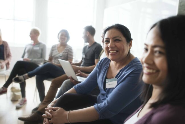 Smiling group participants sit on chairs in a semi-circle