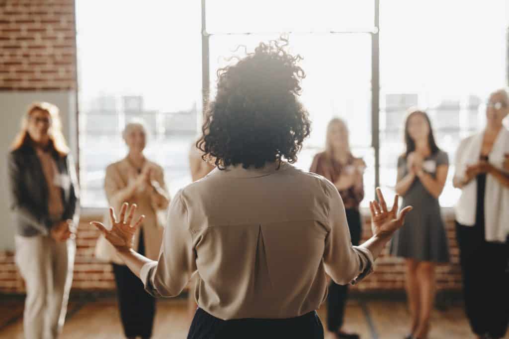 A woman with her back to the camera presents to a group of women.