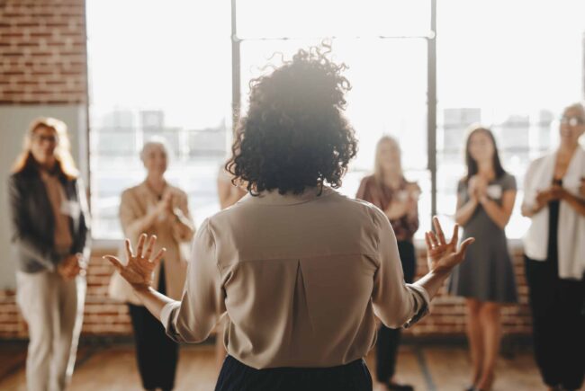 A woman with her back to the camera presents to a group of women.